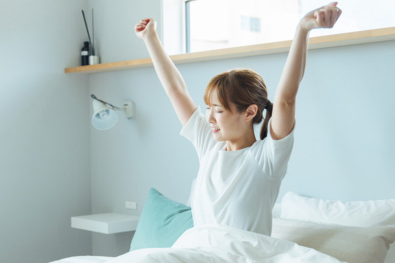 朝、寝起きにベッドで体を伸ばす女性